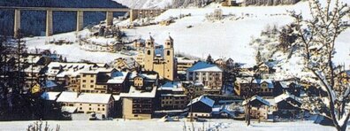 Schneebedeckte Stadt Steinach mit mehreren Gebäuden, zwei markanten Türmen und einer Brücke im Hintergrund.